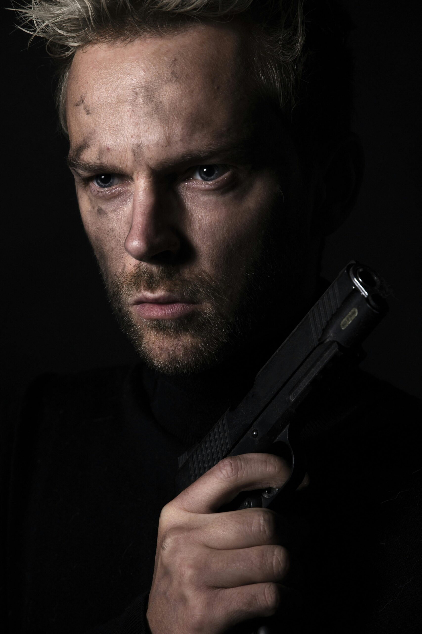 Dark, intense studio portrait of a man holding a handgun, projecting a mysterious feel.